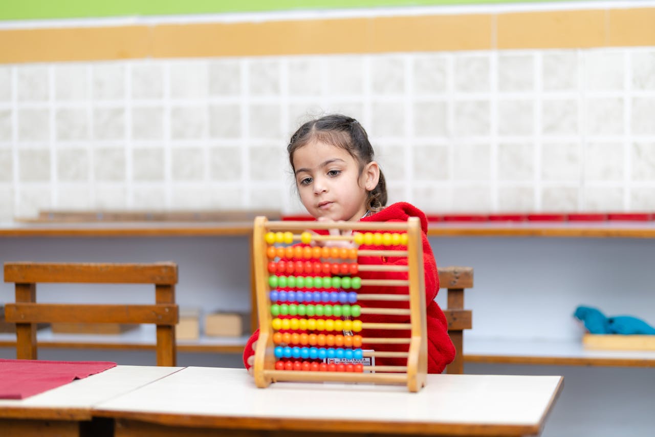 Young child uses colorful abacus in a bright classroom setting.