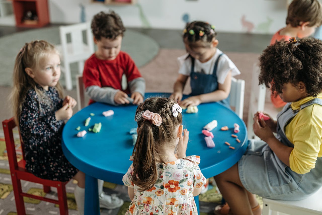 services-04 Group of preschool children playing with clay at a colorful table in a classroom.