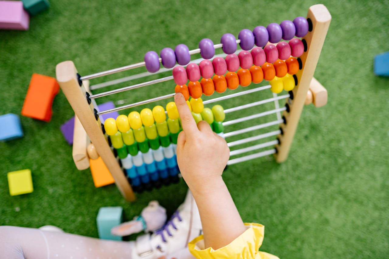 contact-img A child's hand using a colorful wooden abacus on green turf, emphasizing playful learning.